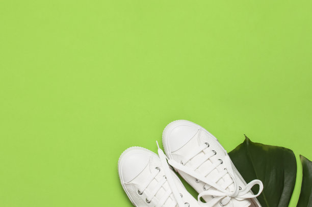 白色女性时尚运动鞋，热带树叶在绿色背景。平面俯视图拷贝空间。女性的鞋子,配饰。时尚的白色运动鞋。夏天创意概念图片下载