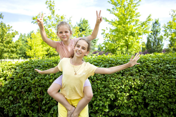 两个学龄女孩姐妹互相拥抱。他们又笑又闹。在夏日城市公园散步。家庭中的爱和友谊图片下载