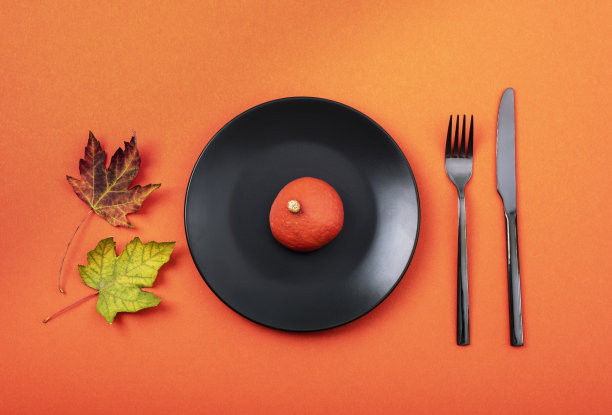 秋季餐桌摆放与黑色盘子南瓜在橙色背景。感恩节，万圣节装饰。俯视图，平铺图片下载