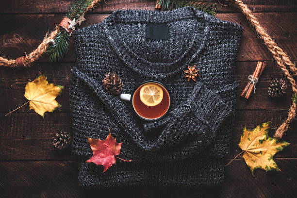 温暖的毛衣，松果，一杯热茶，柠檬，肉桂和大茴香星和秋天的枫叶在木制背景。秋天的衣服和饮料。秋天的概念图片下载