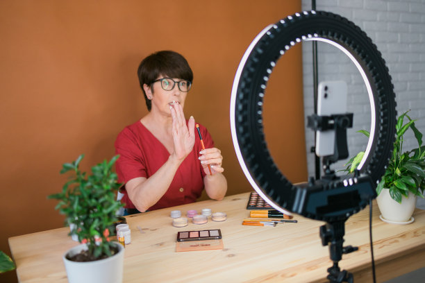 中年女性美妆博主或网红在家中使用环形灯和智能手机录制美妆产品视频图片下载