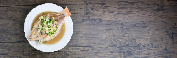 清蒸罗非鱼配辣椒，大蒜和柠檬酱，香草和蔬菜，木桌盘，鱼蒸青柠。泰国中餐图片下载