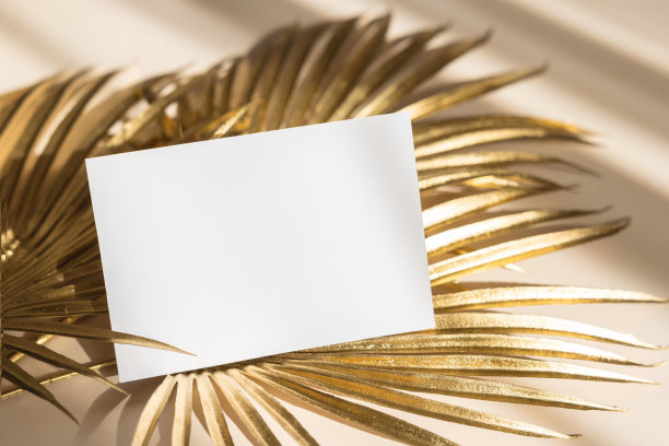 邀请卡模型与金色棕榈叶米色粉彩背景。俯视图，平面布局，复制空间。模板空白的白纸模型为品牌和广告图片下载