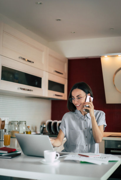 现代的学生。可爱时尚的自由职业女性戴着眼镜，在笔记本电脑上使用手机，在家办公。远程教育与在线教育工作。图片下载