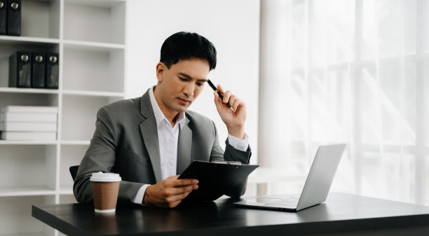 年轻的商人在办公室用笔记本电脑、平板电脑和在纸上做笔记。图片下载