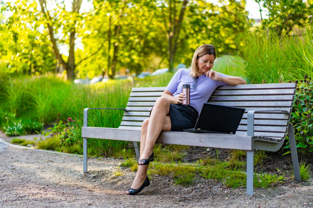 漂亮的中年女人坐在城市公园的长椅上用笔记本电脑图片下载
