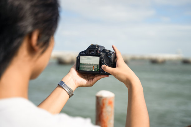 一个男孩在海边用相机拍照图片下载