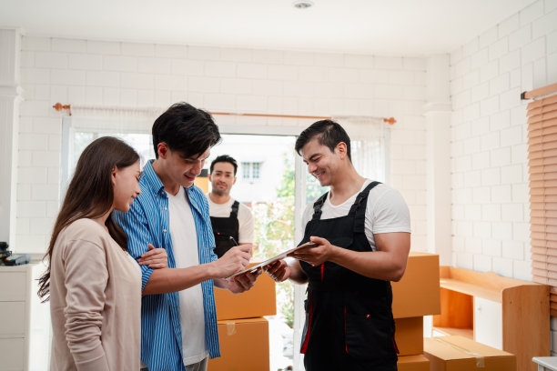 一对亚洲夫妇一边检查，一边把箱子和家具从一辆小货车上卸到一所有服务货物的新房子里，两名穿着制服的搬运工搬运箱子。搬家和送货的概念。图片下载