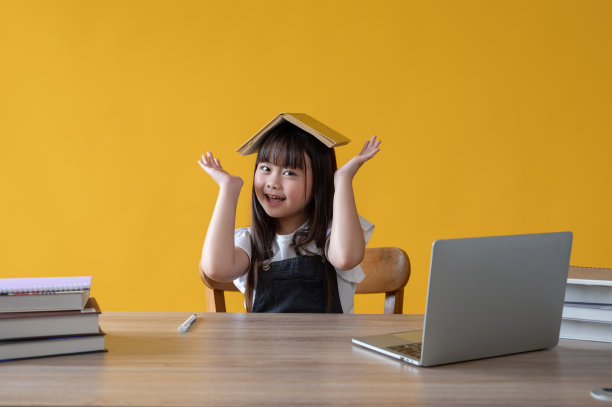 一个开朗可爱的年轻亚洲女孩，头顶一本书，对着镜头微笑图片下载