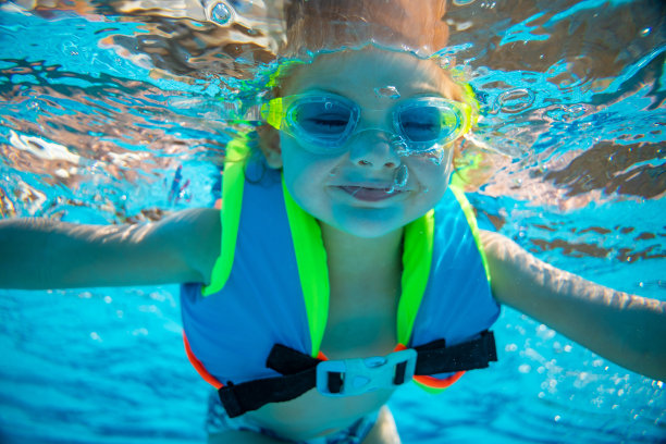 小女孩戴着护目镜和背心在游泳池里游泳的照片。暑假图片下载