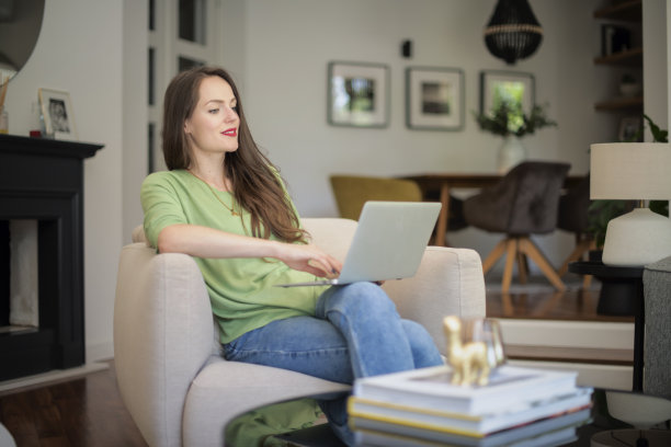迷人的微笑女人坐在扶手椅上使用笔记本电脑图片下载
