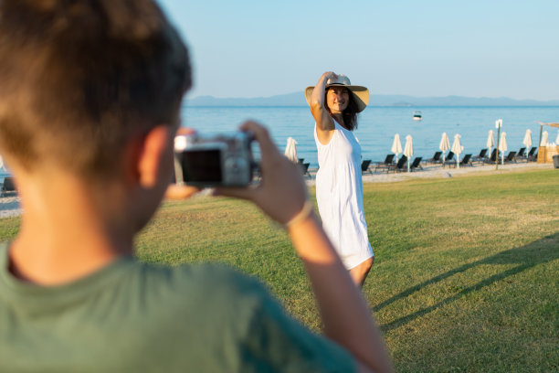 男孩正在海滨附近的公园里给他的妈妈拍照。家庭度假。图片下载