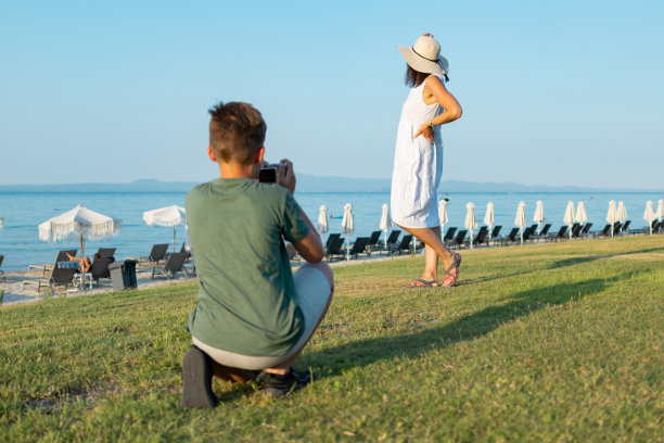 男孩正在海滨附近的公园里给他的妈妈拍照。家庭度假。图片下载