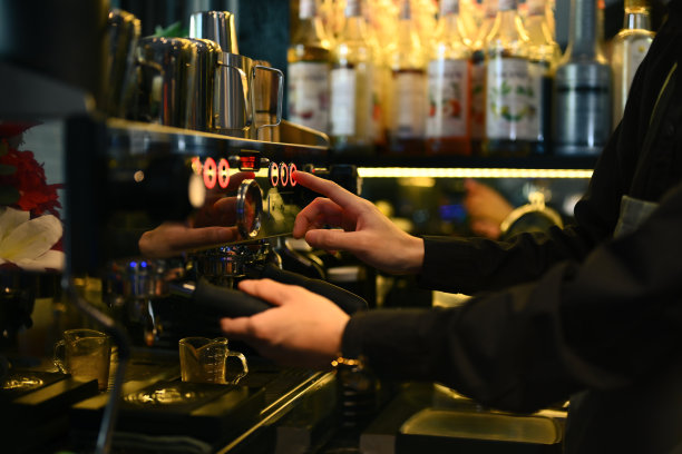 裁剪的咖啡师穿着围裙，在一家时髦的咖啡馆里使用咖啡机为客户制作浓缩咖啡图片下载