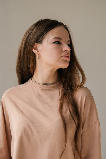 漂亮的年轻女子，一头长发，身穿米色t恤，表情严肃图片下载