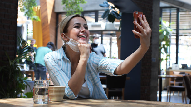 快乐的年轻女子在咖啡馆里自拍。一个快乐的女人用现代智能手机拍照的肖像。图片下载
