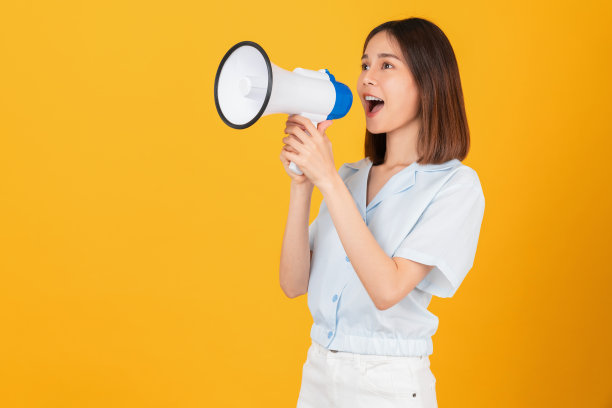 美丽的亚洲女人拿着扩音器，握紧拳头庆祝胜利，在黄色背景上表示成功。图片下载