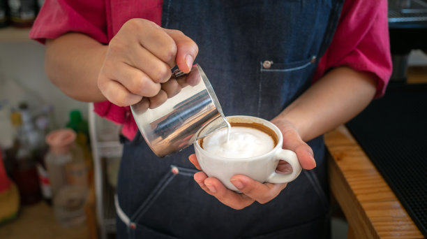 咖啡师在制作卡布奇诺时往咖啡里加牛奶。咖啡师制作卡布奇诺，专业调酒师准备咖啡饮品图片下载
