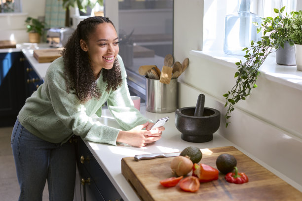 十几岁的女孩在家里的厨房与食材在手机上看食谱图片下载