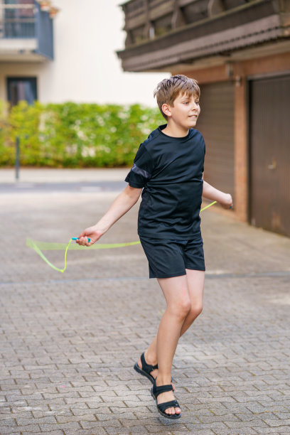 帅气的男孩在户外跳绳。十几岁的男孩在运动营地跳跃和训练。图片下载