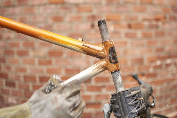 油漆清除:男子在使用喷灯后，在自行车车架上使用钢丝绒图片下载