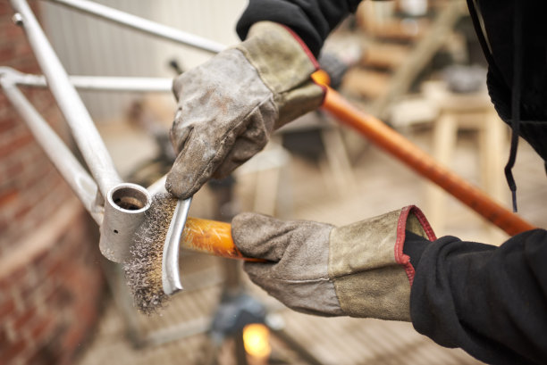 油漆清除:男子戴着防护手套，用钢丝刷在自行车车架上图片下载