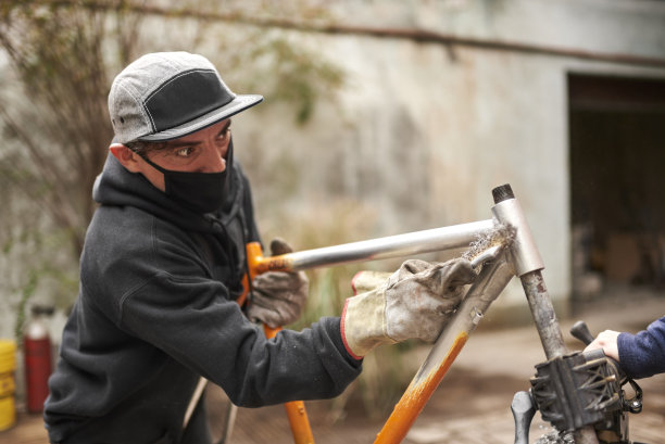 在自行车翻新工作中，一名男子正在清除橙色自行车车架上的油漆图片下载