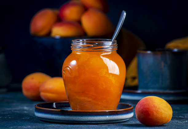 杏果酱或配置在玻璃罐与勺子，新鲜水果在蓝色的桌子背景图片下载