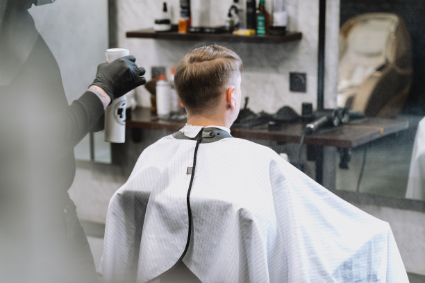 去理发店。时髦的男人发型时尚。理发师、发型师、发型师用剪刀、梳子剪发、梳头。顾客，顾客坐在黑暗的男士美容院披着斗篷图片下载