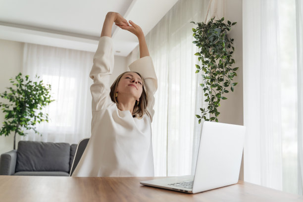 一位年轻的女性在家庭办公室工作，她满意地举起双手微笑着图片下载