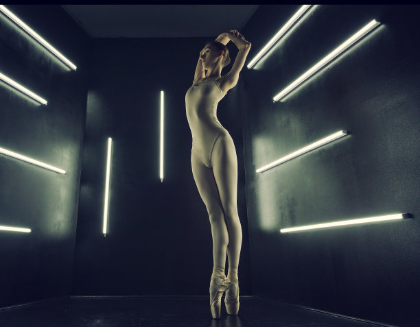 芭蕾舞女演员穿着紧身衣和紧身衣，在昏暗的照相馆灯光下伸展身体图片下载