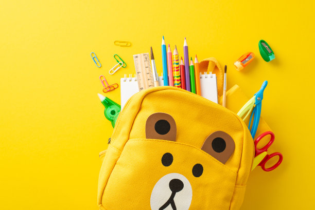 释放乐趣学习的精神与俯视图照片显示各种彩色的学校用品在一个可爱的儿童背包在黄色孤立的背景，完美的文字或广告图片下载