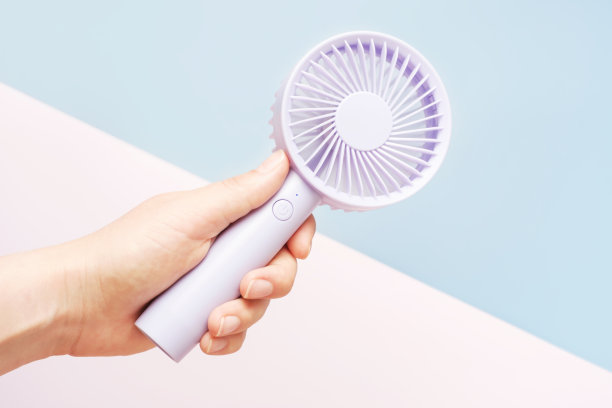 女性手持迷你风扇在蓝色和粉红色的背景特写。图片下载