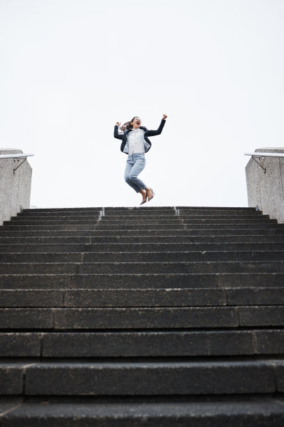 商务人士在楼梯上跳跃庆祝，象征着金融事业的成功图片下载