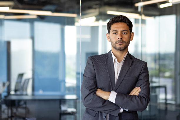 严肃的阿拉伯裔中年商人，在办公室的窗边交叉双臂思考并看着镜头图片下载