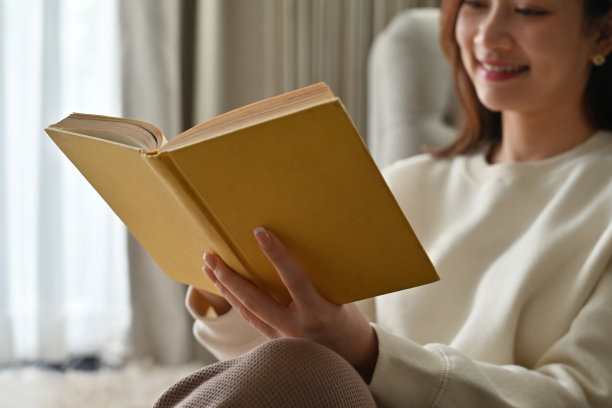 一个快乐的亚洲女人在客厅里享受着一本书，选择性地专注于书。图片下载