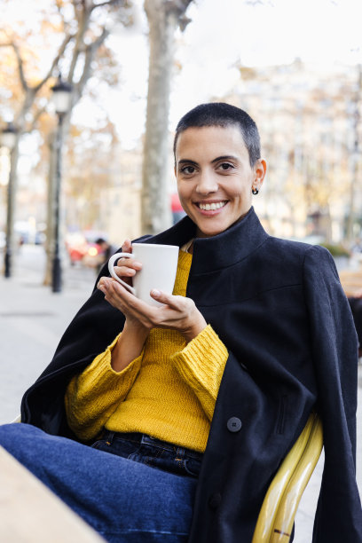 年轻的西班牙妇女光头在城市咖啡馆露台或咖啡店喝咖啡杯;秋天街头的拉丁短发妇女肖像图片下载