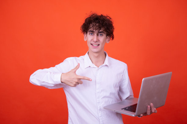 拿着笔记本电脑摆出橙色背景的搞笑人。图片下载