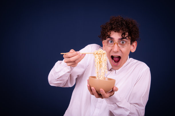 有趣的情绪化的家伙吃中国面条配蔬菜。图片下载