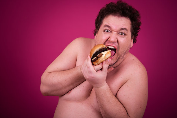 滑稽的胖子正在健身，并且贪婪地吃了一个汉堡包。复古的风格。图片下载