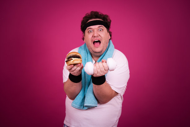 滑稽的胖子正在健身，并且贪婪地吃了一个汉堡包。复古的风格。图片下载