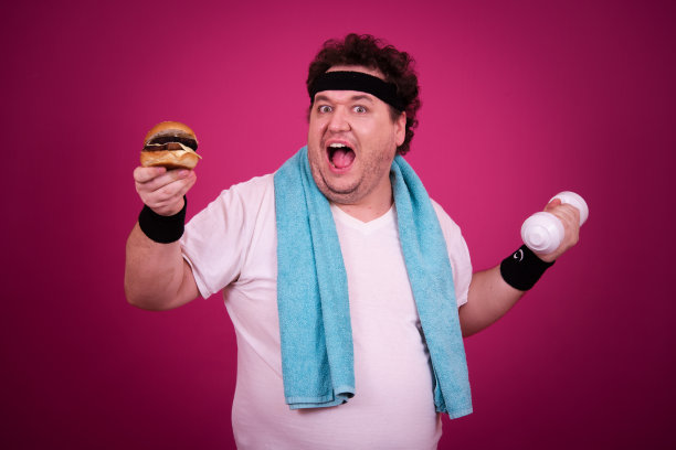滑稽的胖子正在健身，并且贪婪地吃了一个汉堡包。复古的风格。图片下载