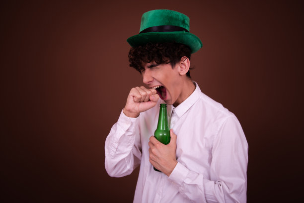 拿着啤酒的搞笑年轻人在棕色背景上摆姿势。图片下载