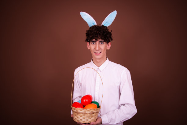 一个有趣的年轻人拿着一篮子鸡蛋在棕色背景上摆姿势。复活节假期。图片下载