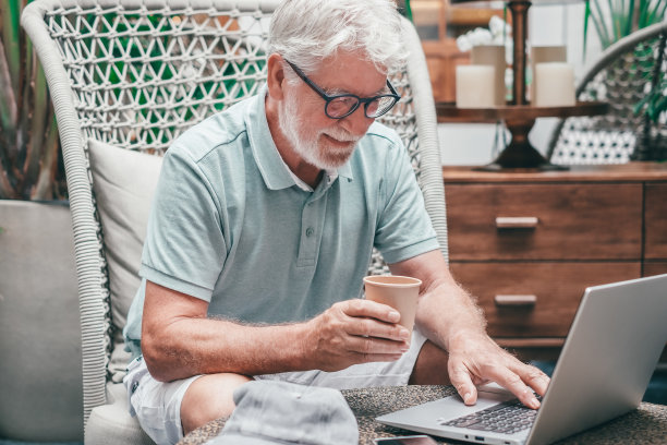 大胡子老头坐在室内，一边上网一边用笔记本电脑打字。喜欢科技和社交的白发老人图片下载