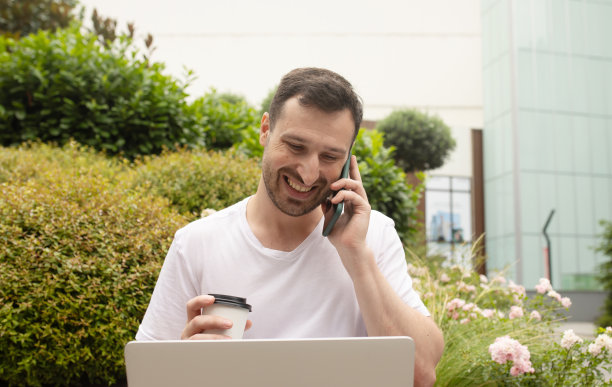 年轻人坐在长椅上浏览笔记本电脑上的数据，喝咖啡去公园做远程项目。图片下载