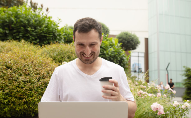 年轻人坐在长椅上浏览笔记本电脑上的数据，喝咖啡去公园做远程项目。图片下载