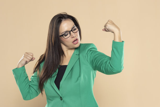 身穿绿色西装的女商人在米色的工作室背景上露出二头肌图片下载