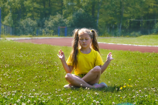 一个穿着黄色夹克的欧洲女孩在体育场的一块绿色空地上沉思。图片下载