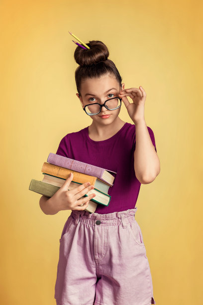 女教师站在黄色背景上。他手里拿着一摞书。她梳着发髻，戴着眼镜。女孩很惊讶。图片下载